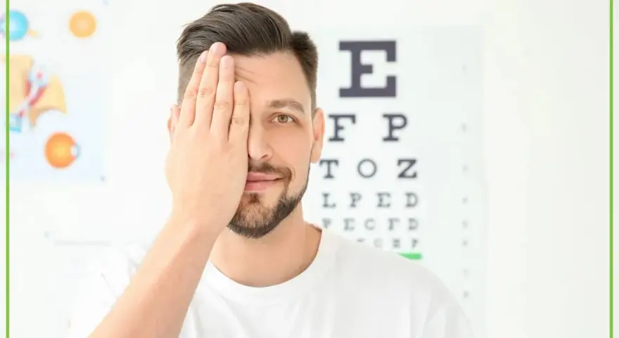 Mężczyzna zasłaniający jedno oko na tle tablicy Snellena.