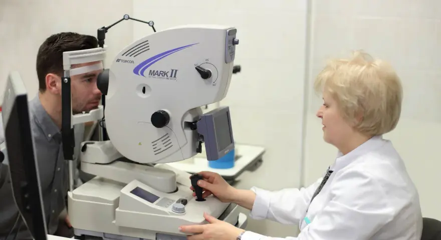 Badanie angiografia fluoresceinowa oka. Pacjent z unieruchomioną głową przed aparatem, okulista obsługuje urządzenie.